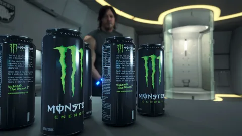 Multiple Monster Energy cans arranged on a table with a person in the background, visually highlighting the tall, recognizable design discussed in the article section
