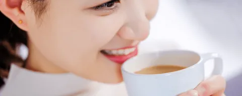 A person smiling while drinking coffee illustrating the action that temporarily softens tooth enamel, making it vulnerable to the acids and pigments in coffee.